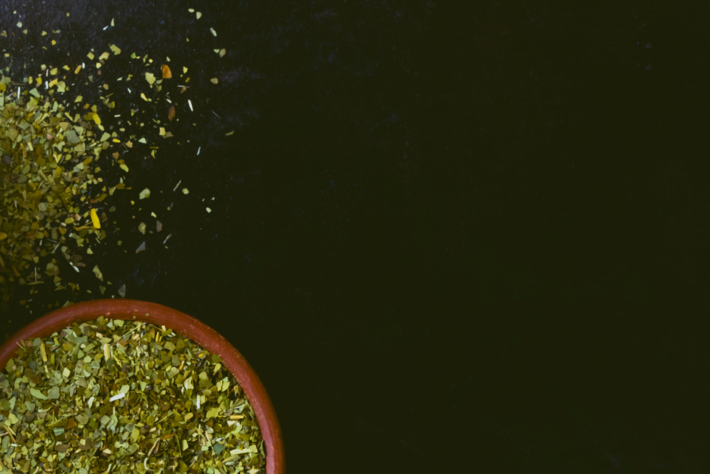 Mediterranean dish with a bowl of green herb salad and a jar of olive oil on a dark surface.